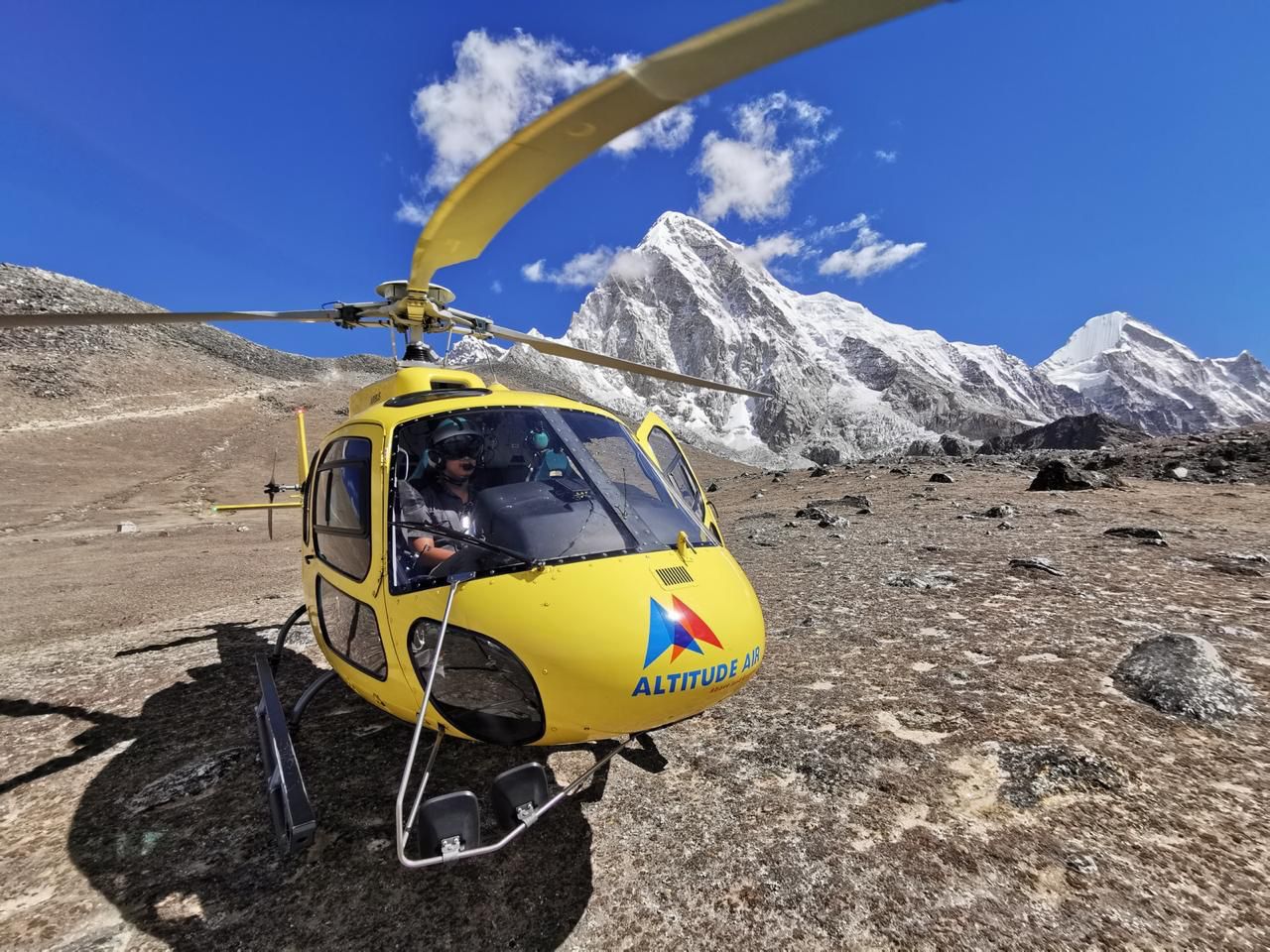 A bright yellow rescue helicopter sits on a rocky, brown plateau with its rotors spinning.