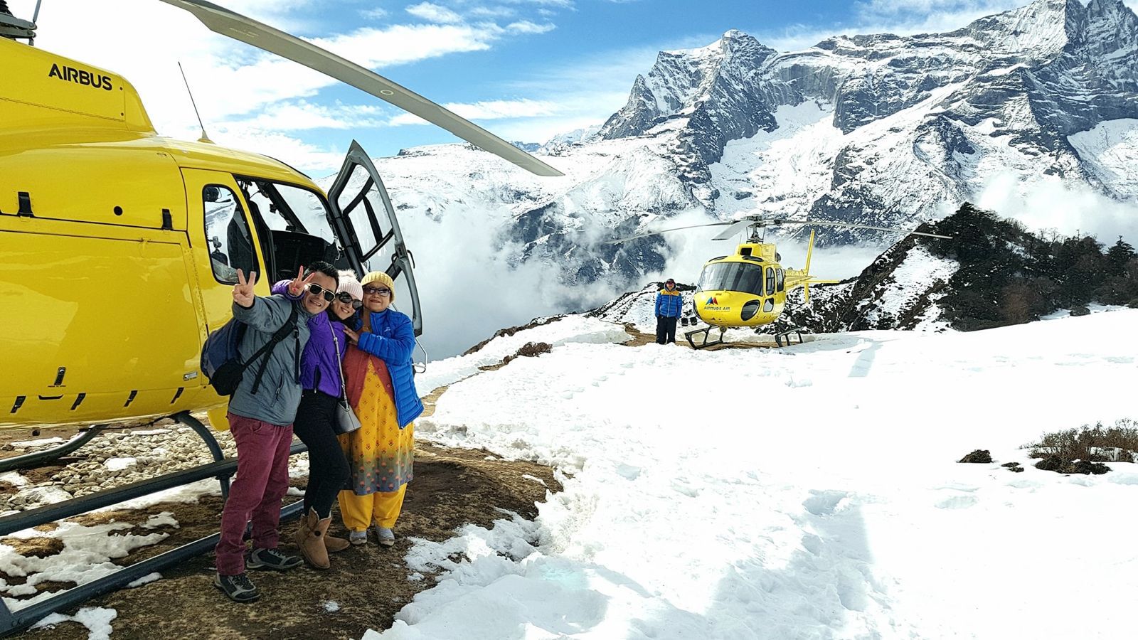 An eye-level medium shot captures a bright yellow Altitude Air helicopter landed on a rugged, rocky plateau in the Himalayas.